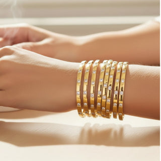 Gold bracelets with embedded stones on a wrist against a neutral background