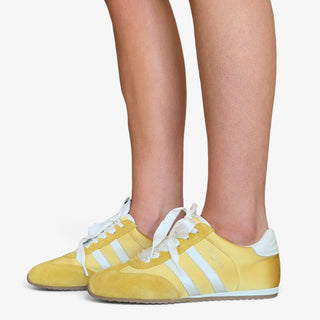 JSlides Peggy yellow sneaker with white stripes and ribbon laces shown on model, side view