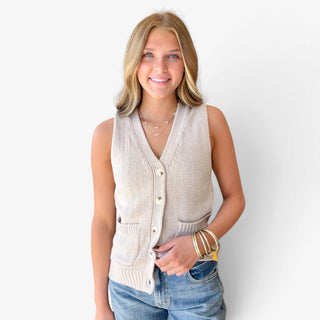  Khaki sweater vest for women featuring a V-neckline, button front, ribbed trim, and front patch pockets, styled with blue jeans, front view.