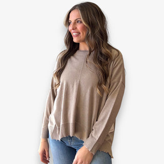 Woman wearing a beige long sleeve top and blue jeans against a white background