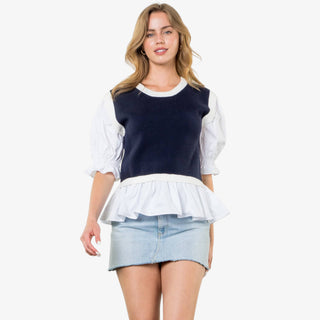 Woman wearing navy mixed media peplum top with white puff sleeves and ruffle hem.
