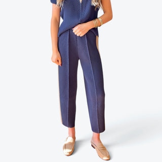 Navy blue pleated tapered pants with diagonal textured fabric, front pleats and ankle-length fit, styled with a matching top, front detail view.