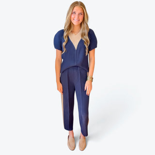 Navy pleated tapered pants featuring a relaxed ankle-length silhouette and textured fabric, styled with a matching navy top, full front view.