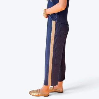 Navy blue tapered ankle pants featuring a contrasting beige side stripe, diagonal pleated texture and relaxed fit, side profile view.