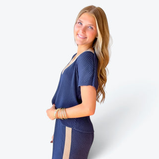 Navy blue pleated short sleeve blouse featuring a relaxed silhouette, textured diagonal pattern and beige V-neck inset, side profile view.