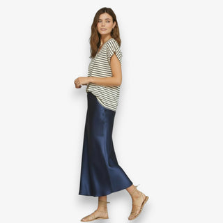 Women wearing a navy satin midi slip skirt styled with a striped t-shirt and sandals on a white background