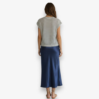 Women wearing a navy satin midi slip skirt styled with a striped t-shirt and sandals on a white background