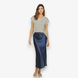 Women wearing a navy satin midi slip skirt styled with a striped V-neck t-shirt and sandals on a white background