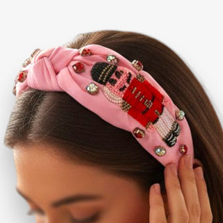Pink headband with a beaded nutcracker design worn by a person on a white background
