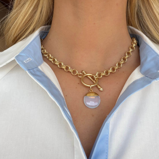 Gold opal pendant necklace with textured chain, toggle closure and round faceted opal-style pendant, shown worn in a close-up front view