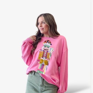 Woman wearing a pink sweatshirt with a colorful nutcracker design on a white background