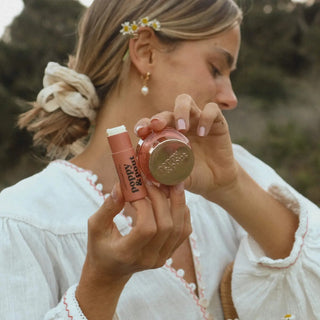 Woman holding Poppy & Pout Pomegranate Peach lip balm and lip scrub outdoors showing the two-piece lip care set
