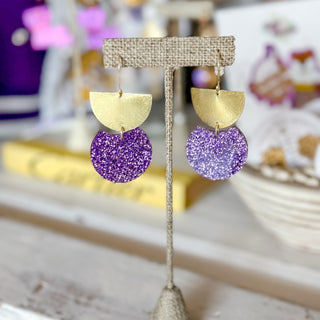 Purple and gold glitter game day earrings with brushed gold geometric drops displayed on an earring stand, front view