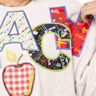 Close-up of Queen of Sparkles teacher sweatshirt showing C and H appliqué with math, chalkboard, floral and classroom graphics with sequins