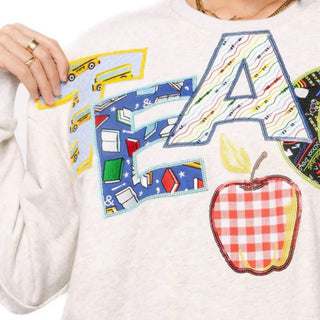 Close-up of Queen of Sparkles teacher sweatshirt showing school bus, book and crayon appliqué letters with gingham apple and sequins