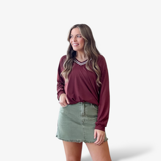Woman wearing a maroon long-sleeve top and green skirt on a white background