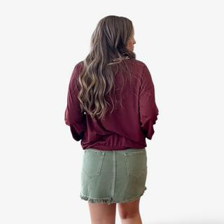 Person wearing a maroon jacket and green denim skirt on a white background