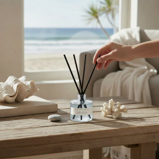 Salt and Sea reed diffuser with powder blue glass bottle on wooden table in coastal beach house living room with ocean view and neutral decor