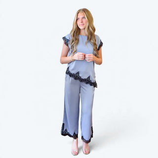  Model wearing a light blue satin lace trim pant set with black lace accents, cropped wide leg pants, and metallic heels, full front view.