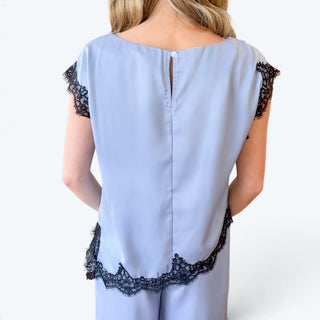 
Back close-up of light blue satin lace trim pant set featuring a button keyhole closure, black floral lace cap sleeves, and scalloped lace hem.