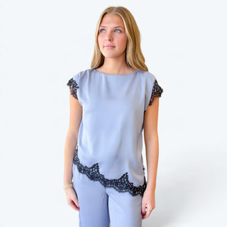 Close-up front view of light blue satin short sleeve top with black lace sleeve accents and scalloped asymmetrical lace hem.