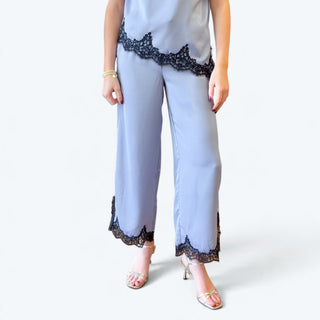 Front detail of light blue satin cropped wide leg pants with delicate black floral lace trim along the hems, styled with metallic heels.