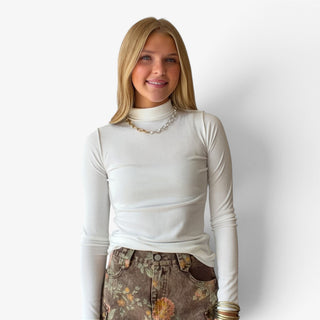 Model wearing  a fitted white turtle neck with long sleeves and brown floral bottoms