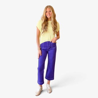 Soft yellow knit top styled with purple cropped wide leg pants and neutral sneakers, full front outfit view.