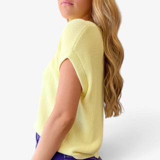Soft yellow knit top with relaxed cap sleeves and ribbed trim, shown from the side with purple pants.