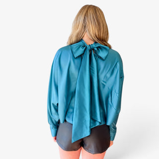 Women's teal satin tie back blouse featuring an oversized statement bow at the back neckline with long flowing ties, full back view.