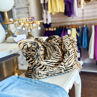 Tan and black tiger print weekender duffle bag with top handles, fringe trim and tassel detail, side front view