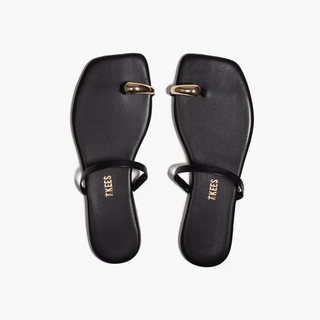 Pair of black sandals with gold toe strap on a white background