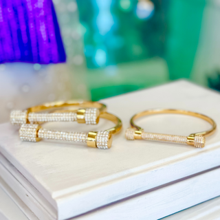 A gold-plated titanium cuff bracelet with sparkling cubic zirconia accents, displayed on a white surface.