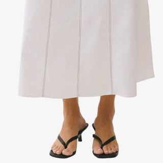 Ivory high waisted maxi skirt with vertical contrast stitching and A-line silhouette styled with black heeled sandals