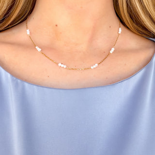 Triple pearl choker necklace with white pearl clusters on a delicate gold chain, styled on a model with a light blue top, front view.