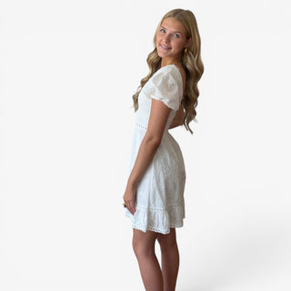 White eyelet mini dress with fitted waist and ruffle hem shown in a side view on model