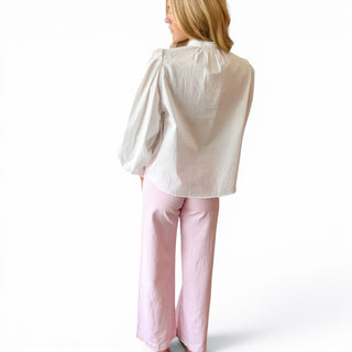 White pintuck cotton blouse with gathered shoulders, relaxed fit and long puff sleeves styled with pink pants, back view.