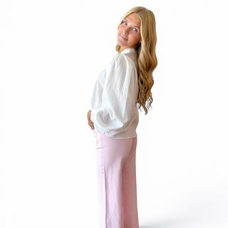 White pintuck cotton blouse with relaxed silhouette and voluminous long sleeves styled with pink pants, side view.