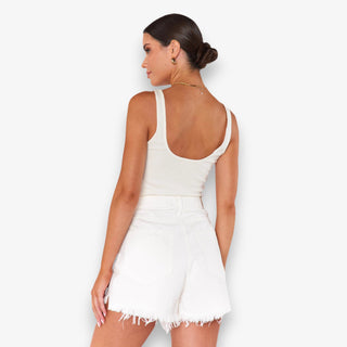 Woman wearing a white sleeveless top and shorts on a plain background