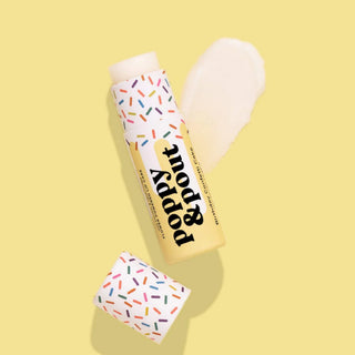 Poppy & Pout Birthday Confetti Cake lip balm opened on a pastel yellow background with nourishing lip balm swatch and colorful sprinkle design.